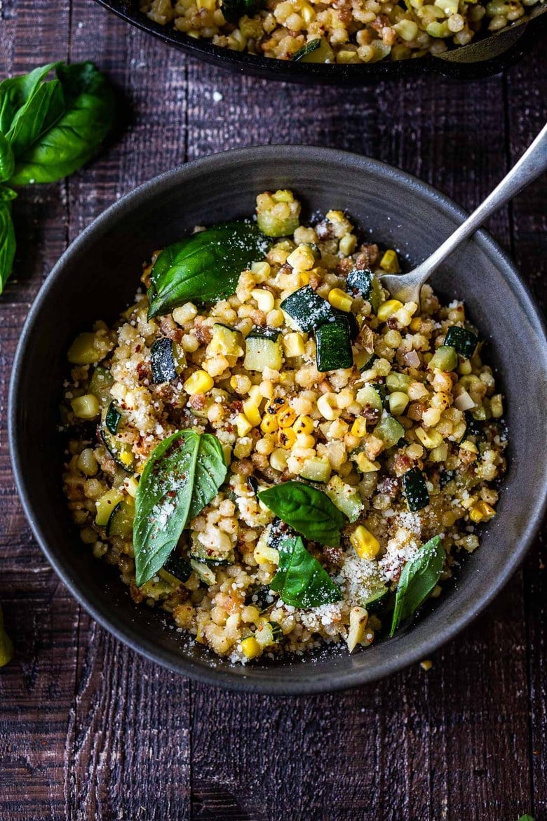 Fregola with Corn, Zucchini and Basil, sprinkled with pecorino in bowl with fork. 