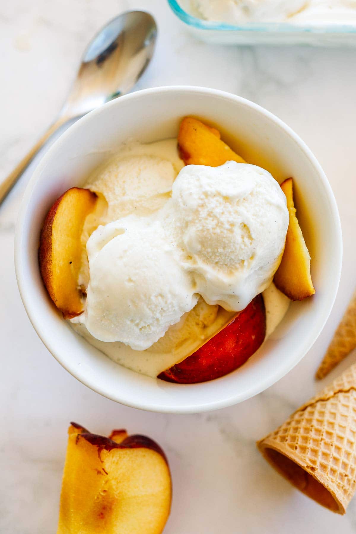 homemade ice cream in bowl with sliced peaches surrounded by ice cream cones. 