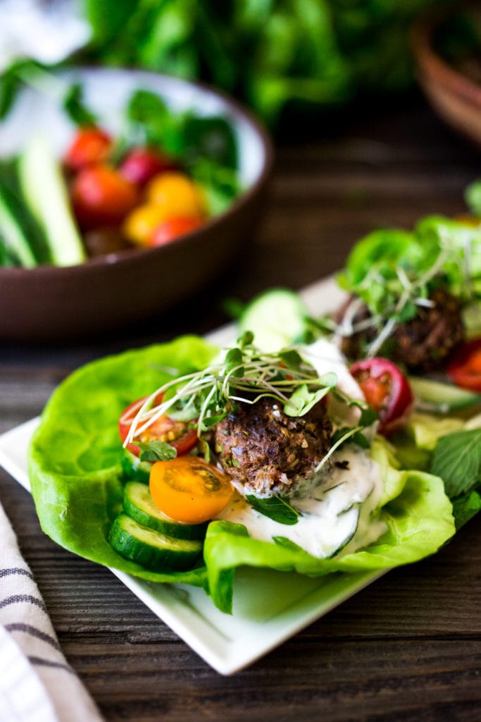 Grilled Lamb Kofta Wraps on serving platter served with tzatziki sauce, sliced cucumber and cherry tomatoes, topped with microgreens. 