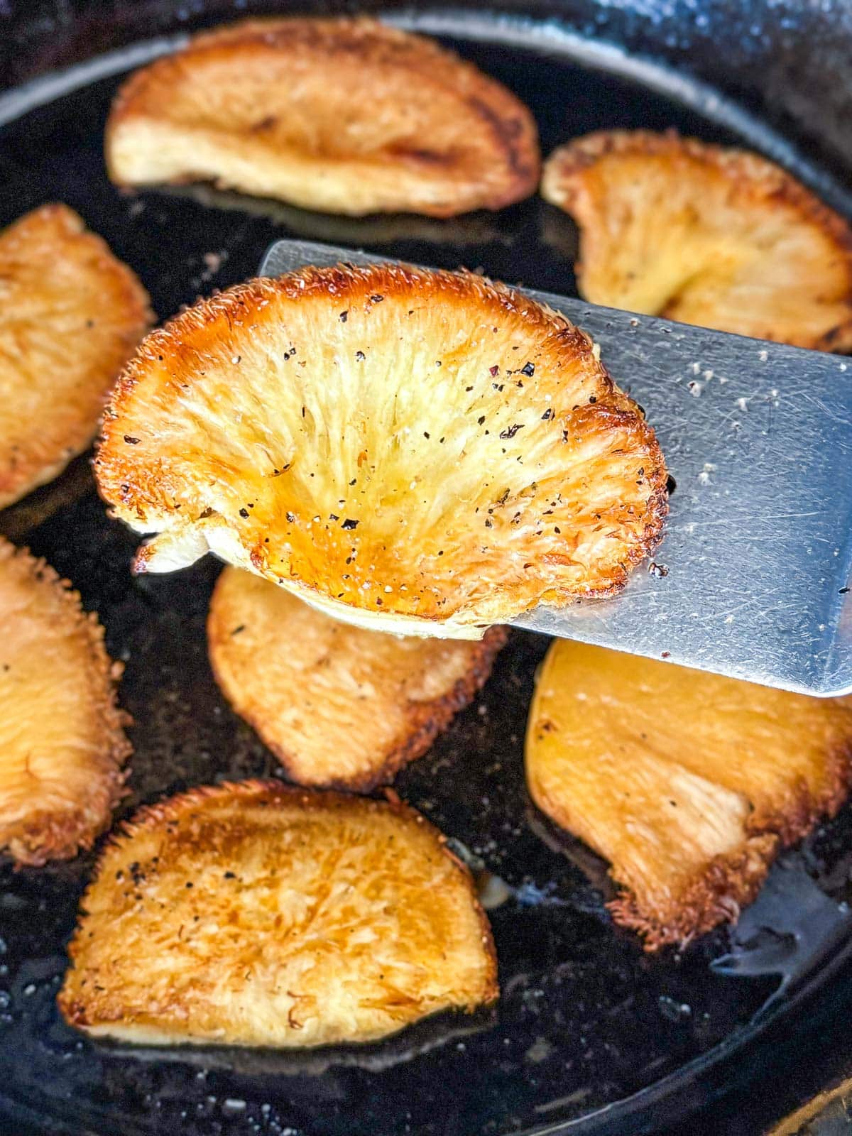 metal spatula holding up seared lion's mane above skillet. 