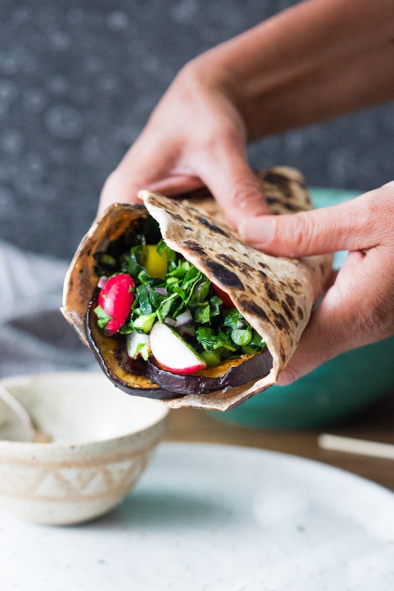 hands holding a middle eastern eggplant wrap stuffed with grilled eggplant and lemony kale slaw. 