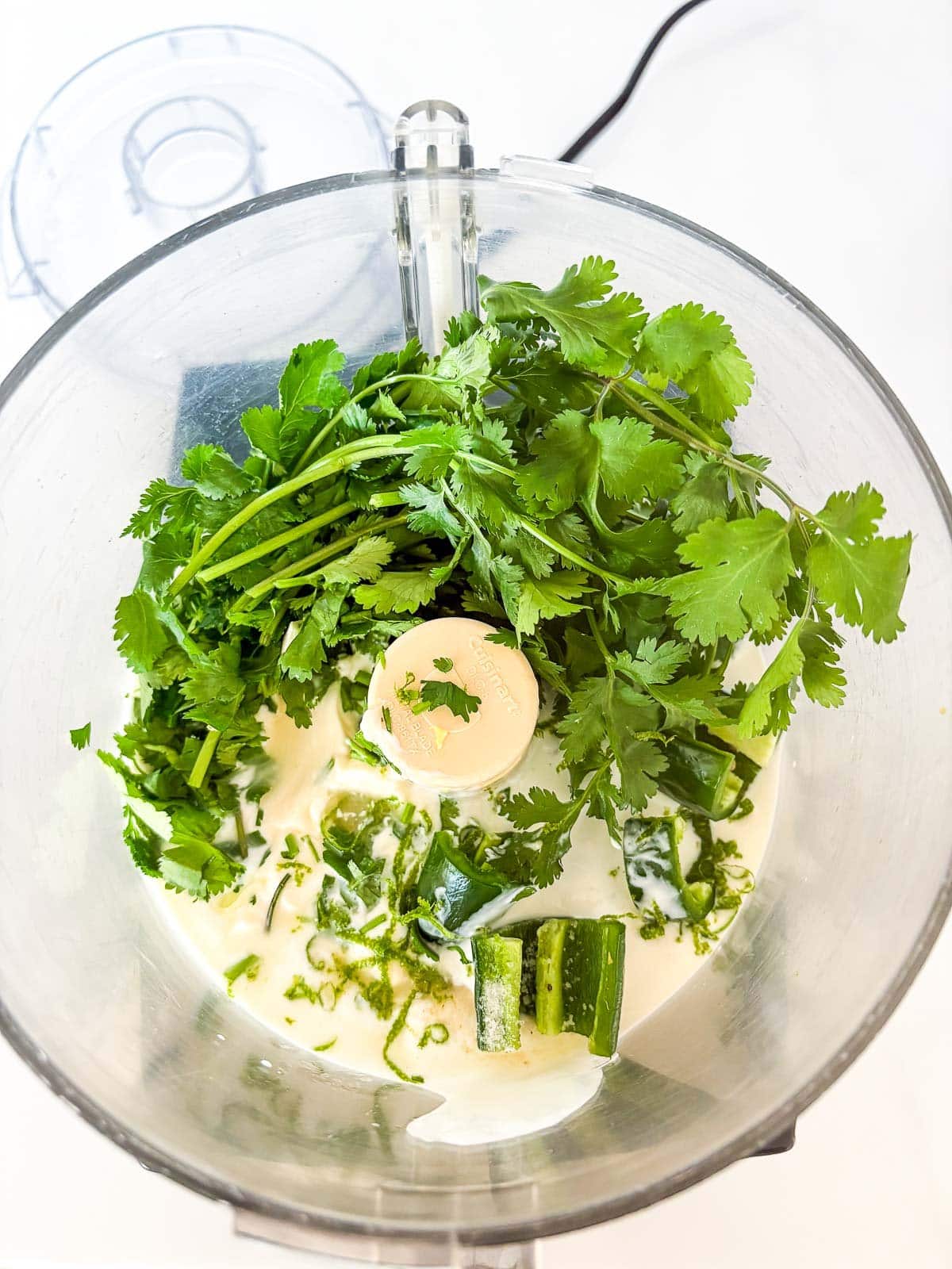 cilantro lime crema ingredients added to bowl of a food processor. 